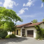 Image de l'extérieur d'une maison mise à la vente dans un cadre arboré et un beau ciel bleu
