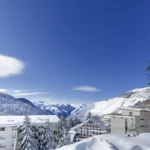 Vue sur les Pyrénées enneigées et le ciel bleu avec quelques bâtiments de station en premier plan