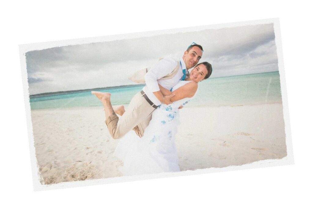 Photo d'un couple, la mariée soulevant dans ses bras son époux sur une plage de sable blanc