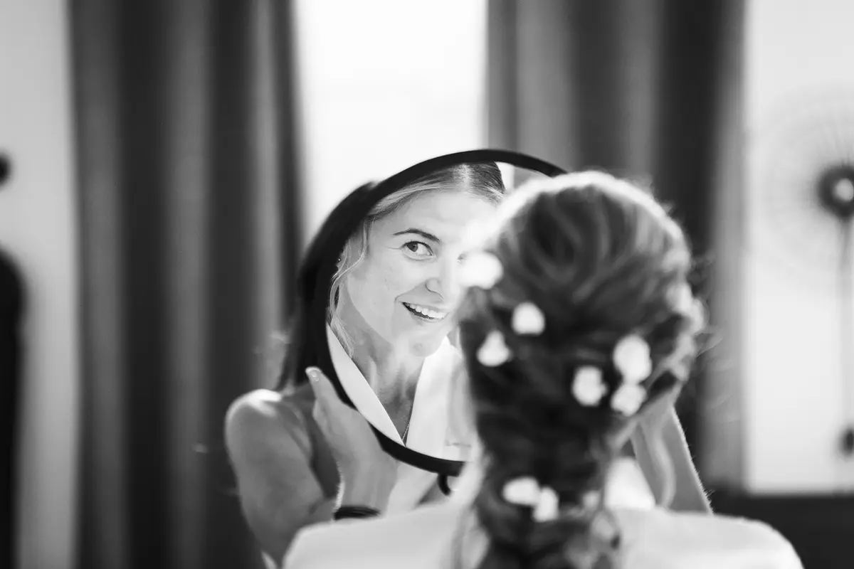 Photo en noir en blanc où l'on distingue le reflet de la mariée observant sa coiffure dans un miroir