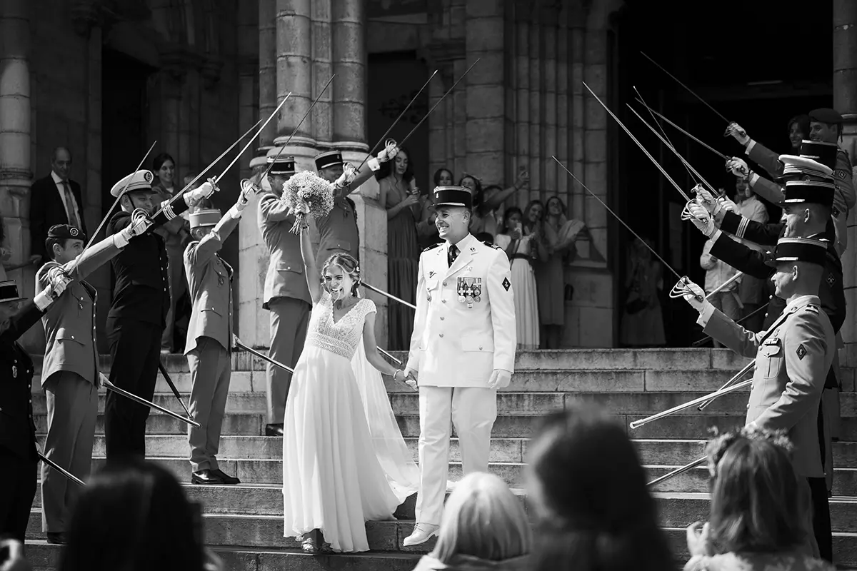 Photo en noir et blanc des mariés à la sortie d'une église à Pau, ils passent sous une haie d'honneur formée par des militaire en costume brandissant leur épées