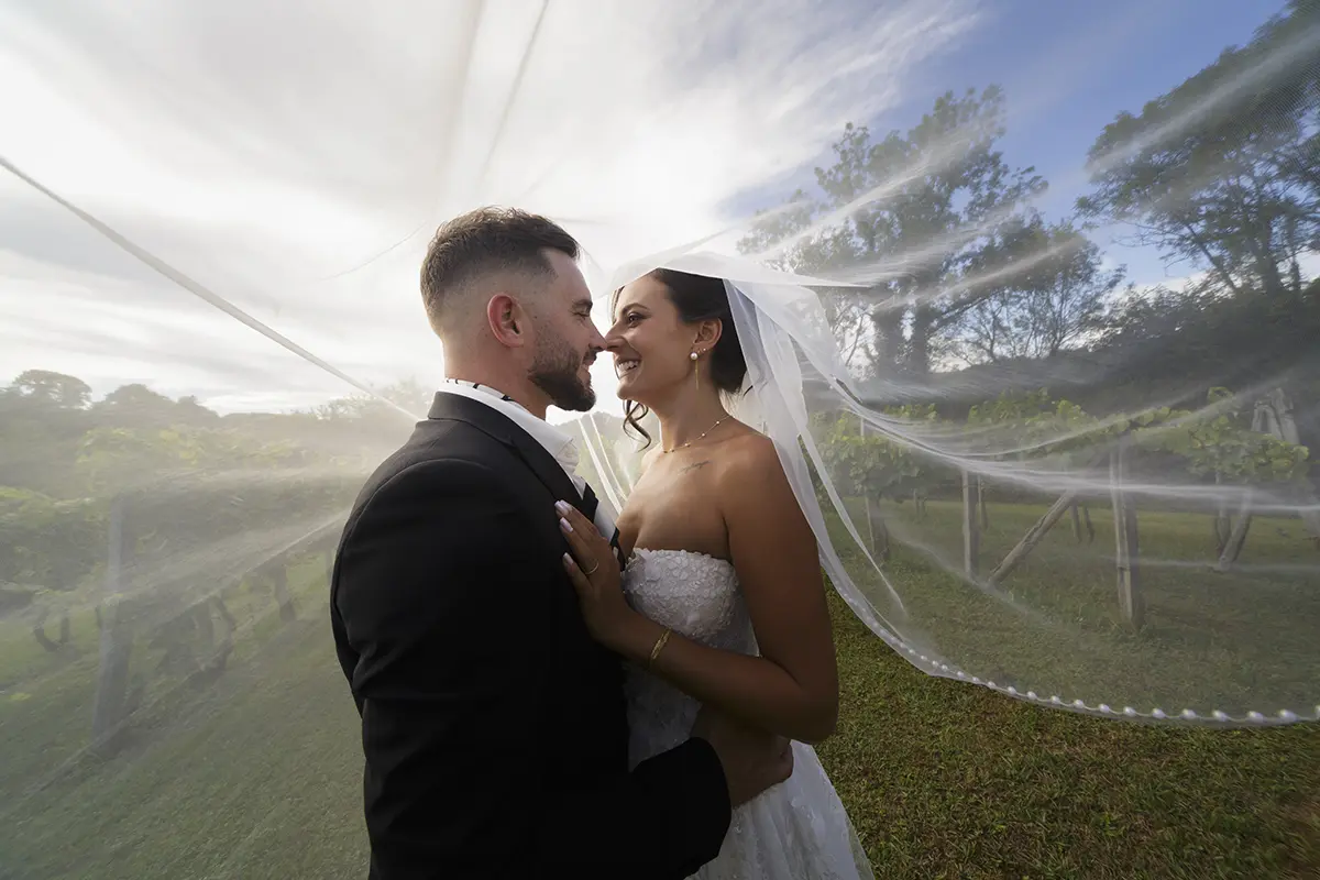 Photo de deux mariés s'enlaçant sous le voile de la mariée dans les vignes