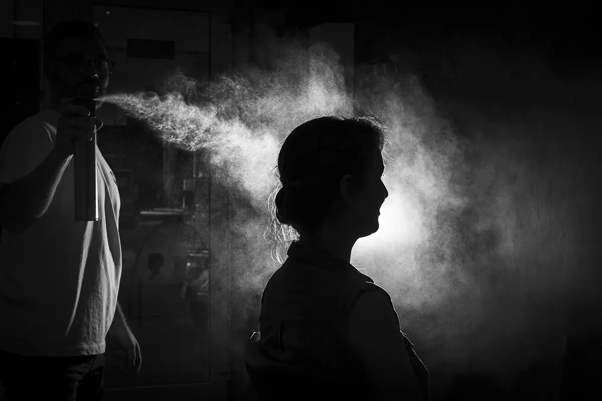 Photo en noir et blanc où l'on distingue simplement la silhouette de la mariée se faisant aspergée de laque, formant ainsi un nuage de lumière